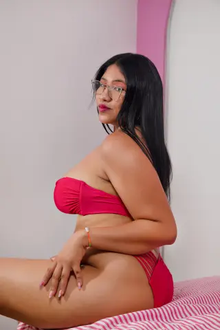 Young woman in red bikini sitting on a pink striped bed in a bright, minimalist room.