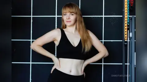 Blonde woman in black sports bra and leggings posing confidently in a modern gym setting.