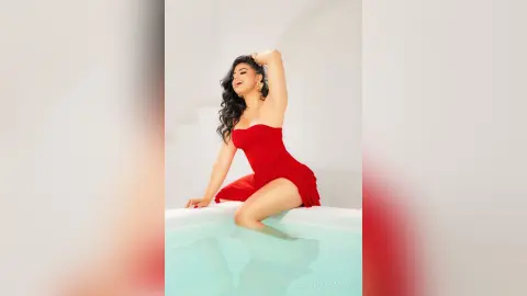 Cheerful woman in a red cocktail dress relaxing in a luxury white bathtub for a glamorous lifestyle shoot.