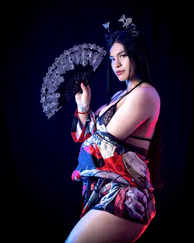 Woman in patterned red and black robe holding a lace fan against a dark background.
