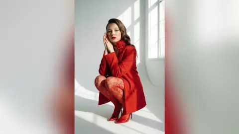 Elegant woman in a red blazer and lace tights posing in a bright, minimalist studio setting.