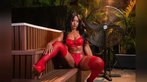 NohomiCambel poses in red lace lingerie and red thigh-high stockings while sitting on wooden steps outdoors at night.