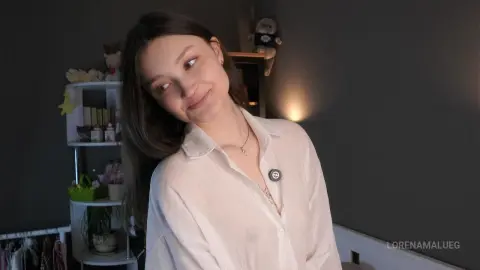 Smiling young woman in a white button-down shirt sitting in a cozy, dimly lit room.