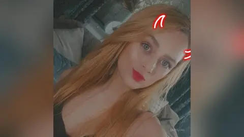 Blonde woman with red lipstick posing for a cozy indoor selfie in a relaxed mood.