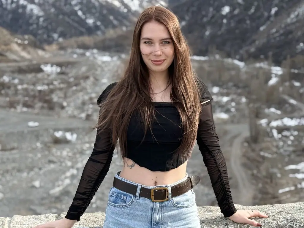 Smiling woman in a black long-sleeve crop top and denim jeans standing in a snowy mountain landscape.