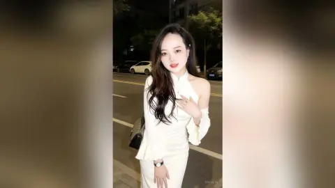 EnyaLin poses outdoors at night wearing a white off-the-shoulder top with long flared sleeves and long dark hair.