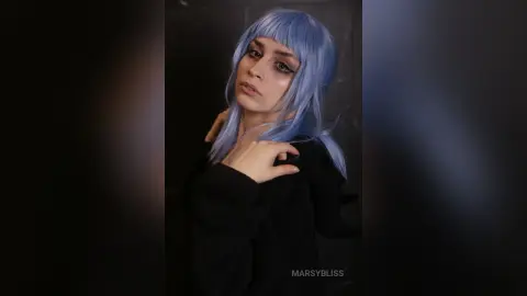 Moody portrait of a woman with lavender blue hair wearing a black sweater in a dark setting.