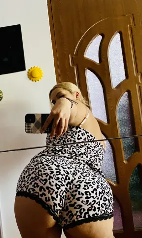 Blonde woman in leopard print sleepwear taking a mirror selfie in a cozy home setting.