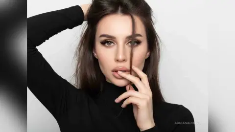 Elegant woman in a black turtleneck posing with a moody, sophisticated expression against a white background.
