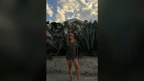 Blonde woman in a dark mini dress posing outdoors near agave plants under a cloudy sky.
