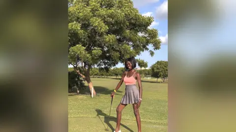 Smiling young woman in a peach tank top and grey mini skirt standing on a sunny green golf course.