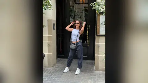 Stylish woman in a white tank top and dark baggy trousers posing outside a classic urban building entrance.