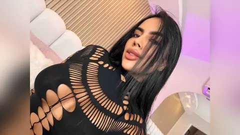 Young woman in a black cutout bodysuit relaxing in a modern bedroom with soft purple lighting.