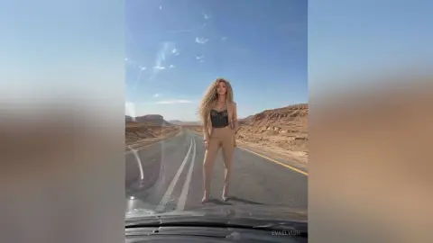 Stylish woman in a beige blazer and corset outfit posing on a desert highway under a bright blue sky.