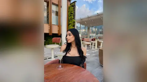 Elegant woman in a black lace top enjoying a cocktail at a sunny rooftop lounge terrace.