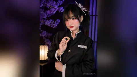 Young woman in black traditional outfit holding a gold coin in a moody purple floral setting.