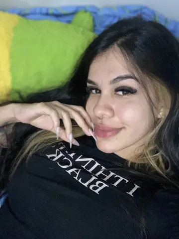 Smiling young woman with long dark hair wearing a black graphic t-shirt while relaxing on a green pillow.