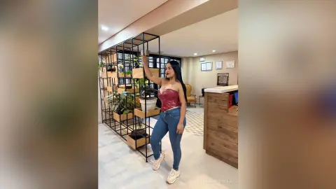 Stylish woman in a red corset top and blue jeans posing in a modern minimalist living room.