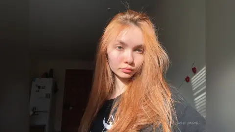 Redheaded woman in a black graphic t-shirt sitting in warm sunlight indoors.