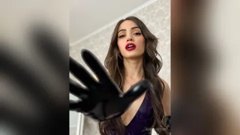 AlienaMoore — AlienaMoore wears black latex gloves and a purple dress while looking into the camera with red lipstick.