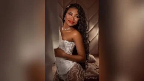Smiling woman in a white corset and patterned leggings posing in a warm, moody indoor setting.