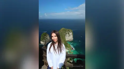 Smiling woman in a white long-sleeve shirt enjoying a scenic ocean view from a coastal cliff lookout.