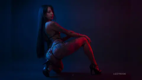 Tattooed woman in black lingerie posing in moody blue and red studio lighting.