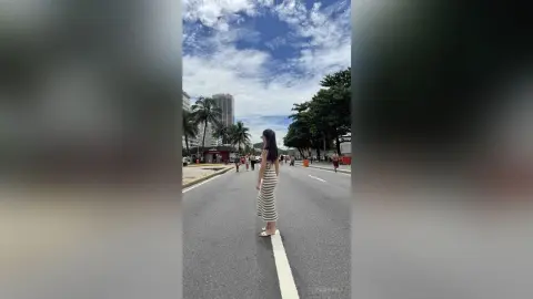Woman in a striped maxi dress standing on a city street under a blue sky.