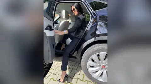 Stylish woman in a black blazer and trousers stepping out of a luxury black SUV on a sunny day.