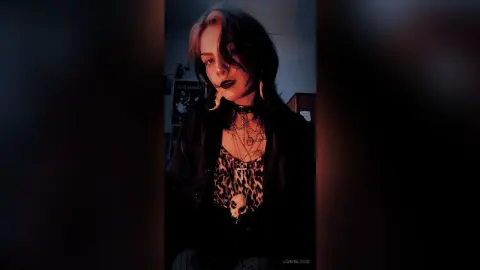 Moody portrait of a woman in gothic aesthetic outfit with layered necklaces and dark makeup in dim lighting.