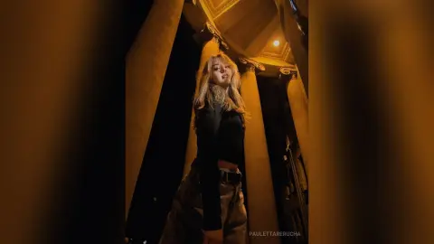 PaulettaRerucha poses in a black long-sleeved top and dark pants against a backdrop of large stone columns.