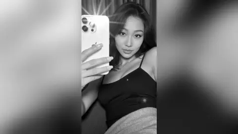 Young woman in a black tank top taking a moody black and white mirror selfie with a smartphone.