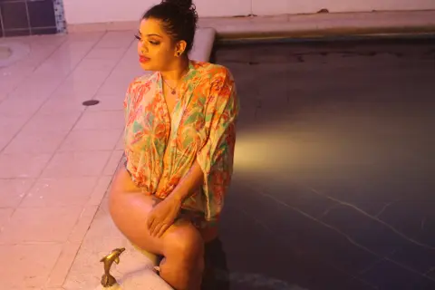 Young woman in a floral patterned kimono sitting by a swimming pool at night in a relaxed mood.