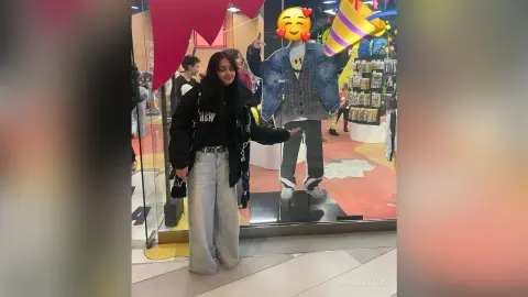 Young woman in a black jacket and wide-leg jeans posing in a bright retail store window.