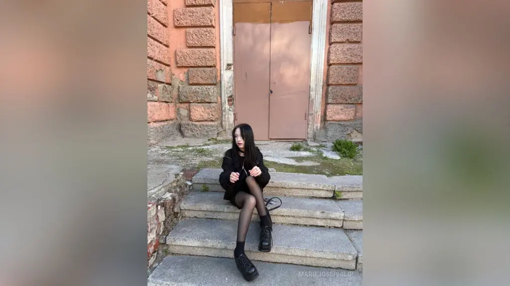 MarieJosePhilip β MarieJosePhilip sits on stone steps wearing a black outfit and sheer black tights with black shoes, posing against a large pink door and stone wall.