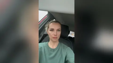 Young woman in a green crewneck sweatshirt sitting in a car with a natural, calm expression.