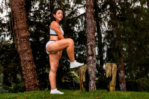 Athletic woman in white fitness outfit posing in a lush green forest setting with a peaceful mood.