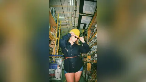 Stylish woman in a navy button-down shirt and yellow beanie posing in a warehouse setting with a cool mood.