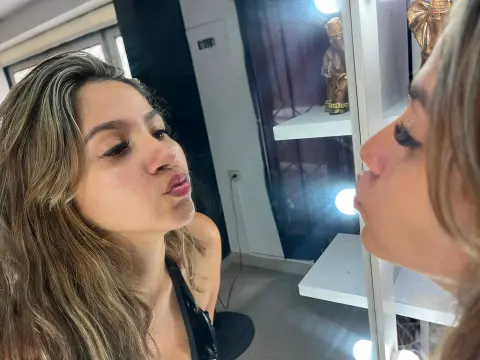 SaraPrincs makes a kissing face while looking into a mirror in a dimly lit room.