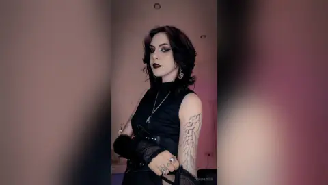 LorenLoiss poses in a black sleeveless top and dark lipstick, showing off her dark hair and arm tattoos.