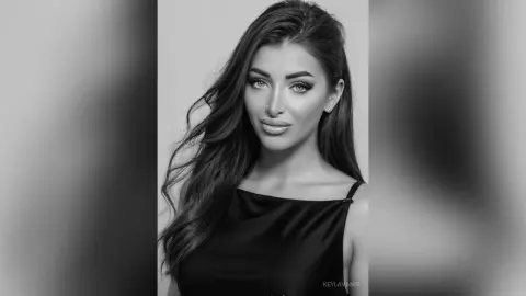 Elegant woman with long wavy hair wearing a black satin top in a moody black and white studio portrait.