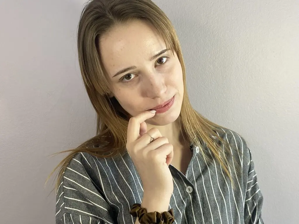 Smiling young woman in a grey striped button-down shirt posing against a plain white wall.