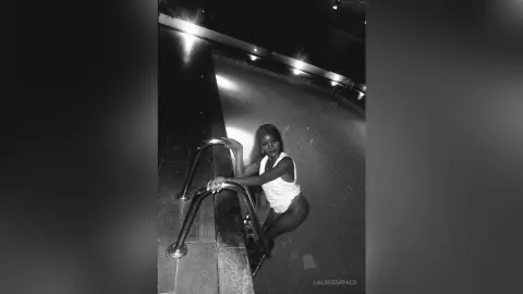Black woman in a white tank top posing by a pool at night in a moody black and white aesthetic.