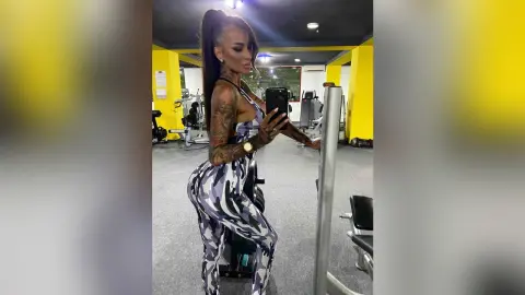 Tattooed woman in patterned gym leggings exercising with weight machines in a bright fitness center.