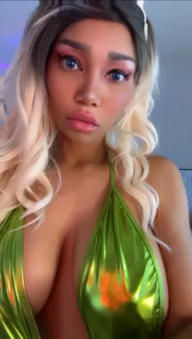 Woman with blonde wavy hair wearing a shiny green halter dress in a soft indoor setting.