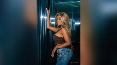 Stylish woman in a brown crop top and blue jeans posing confidently in a modern elevator setting.