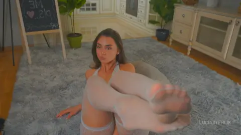 Young woman in white lace lingerie relaxing on a grey shag rug in a bright, cozy living room.