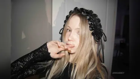 Blonde woman in a black lace top and ruffled headband posing in a moody indoor setting.