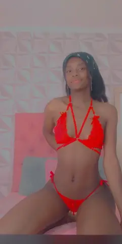 Young woman in a vibrant red bikini sitting on a bed in a bright, modern bedroom.