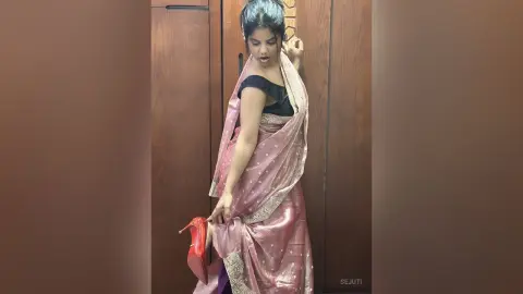 Elegant woman in a shimmering pink silk saree posing gracefully in a modern indoor setting.